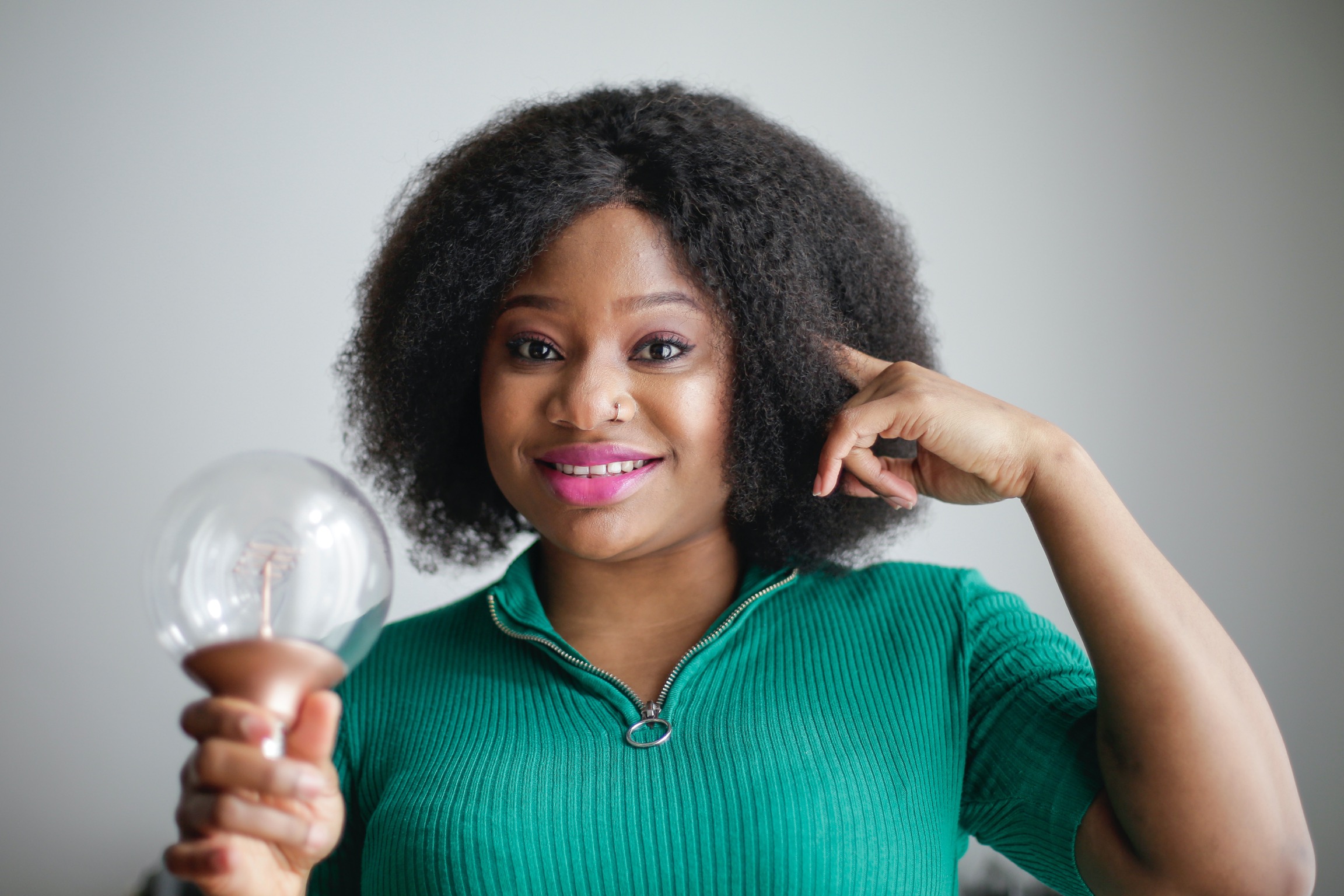 Woman holding a light bulb on one hand and pointing at her head with the other